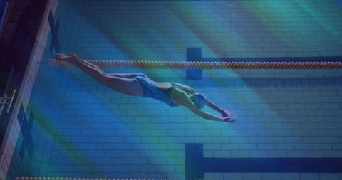 Competitive swimmer gliding underwater along lane rope in illuminated Olympic-style pool