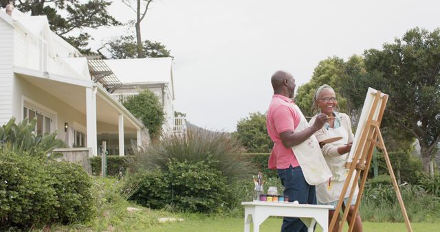 Happy senior african american couple painting picture in garden and talking, copy space. Retirement, togetherness, creativity, hobbies and senior lifestyle, unaltered.