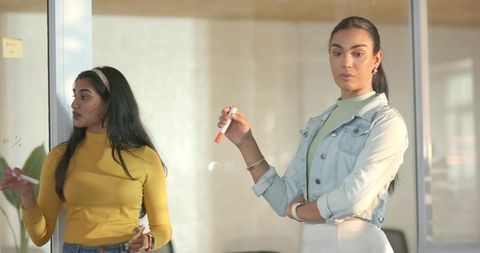Diverse female team collaborating on glass board with colorful sticky notes and markers