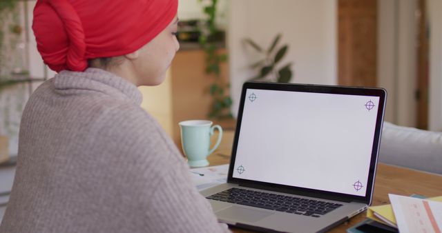 Image of biracial woman in hijab sitting at desk at home, working on laptop, copy space on screen. Remote working, communication, inclusivity and domestic life.