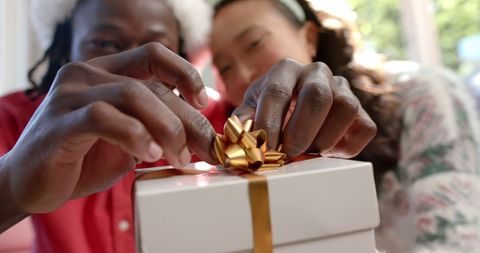 Cheerful couple wrapping christmas gift with golden ribbon