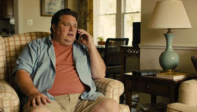 Man talking on smartphone while sitting in cozy daylight living room armchair with lamp