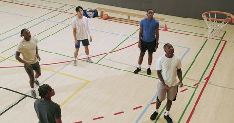 Multiracial men practicing basketball drills on indoor court during casual team training