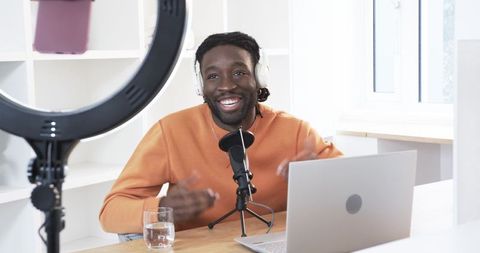 African american creator recording podcast with microphone, laptop and ring light in bright home stu