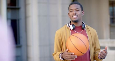 African American college student holding basketball by campus columns wearing headphones