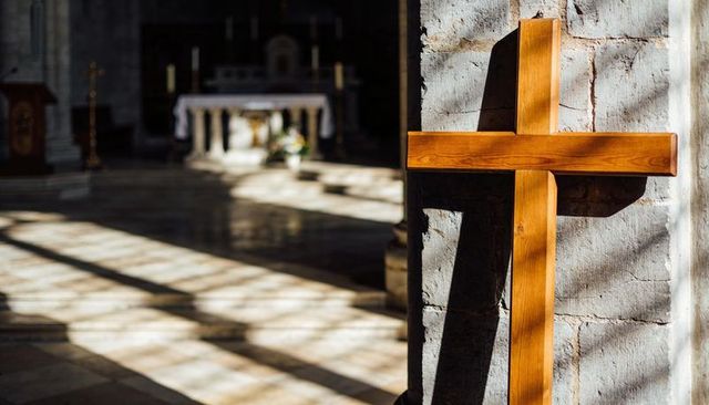 Sunlit wooden cross leaning against stone pillar in historic church nave