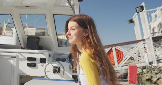 Young woman with long hair is enjoying a sunny day on a boat deck, smiling and looking out to the scene. Use this image to depict relaxation, summer travel, and the joy of being outdoors. Ideal for tourism advertisements, leisure lifestyle articles, or travel-related blogs.