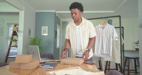 Adult male packing clothing orders at home office table for small business ecommerce