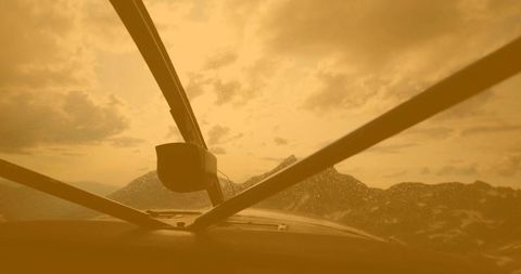 Cockpit windshield view over mountain range showing water droplets and golden light