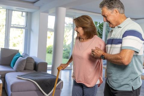 Senior couple practicing home mobility support while partner provides steadying assistance