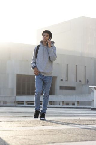 African american young man walking and talking on phone carrying backpack on urban rooftop plaza