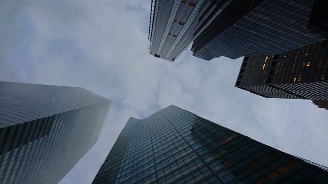 This image depicts a group of modern skyscrapers viewed from below, set against a cloudy sky. It may be used for projects focusing on urban development, modern architecture, business environments, or city landscapes. It can be suitable for articles related to real estate, financial districts, metropolitan lifestyle, or presentations about urban planning and growth.