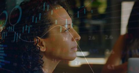 Mature professional woman analyzing financial charts reflected on office monitor glass