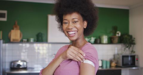 Smiling African American Woman Showing Vaccine Bandage in Kitchen