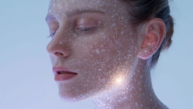 Woman wearing crystalline flakes on face with warm glowing highlights and iridescent sparkle