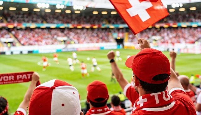 Swiss football fans cheering in stadium waving flag and wearing red-and-white scarves
