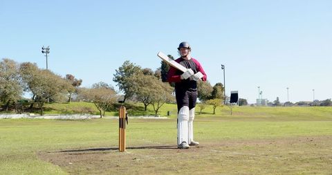 Cricketer Holding Bat on Field Amid Clear Sky Calmness