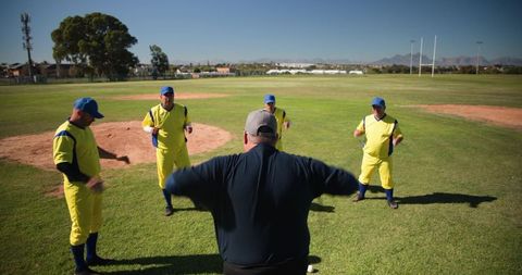 Coach leading men's baseball warm-up with players forming semicircle on sunny grass field