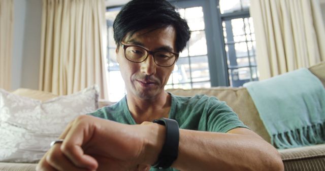 Asian Man Checking Fitness Tracker Sitting on Couch - Download Free Stock Images Pikwizard.com