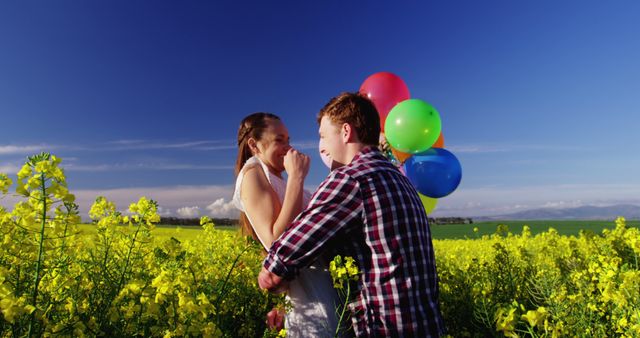 Romantic couple holding colorful balloons and embracing each other in mustard field on a sunny day