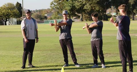 Coach leading outdoor team warm-up stretching and arm swings before practice on grass