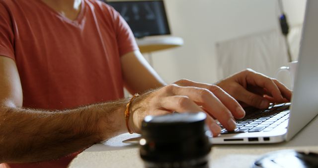 Person typing on laptop at home workspace, focusing on hands on keyboard. Ideal for depicting modern remote work, freelancing, technology use in daily life, casual professional environments. Highlights home office setting and usage of laptop for work tasks, suitable for articles, blogs, and advertisements about remote work, freelancing, or technology.