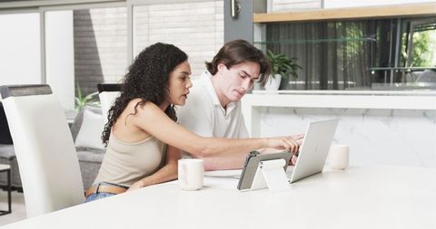 Multiracial Couple Collaborating at Table with Laptop and Coffee