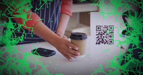 Barista serving takeaway coffee beside QR code display for contactless mobile payment
