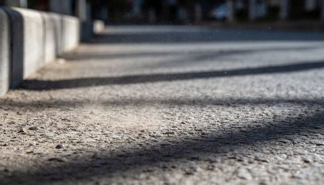Sunlit urban pavement revealing textured asphalt and long linear shadows on concrete curb