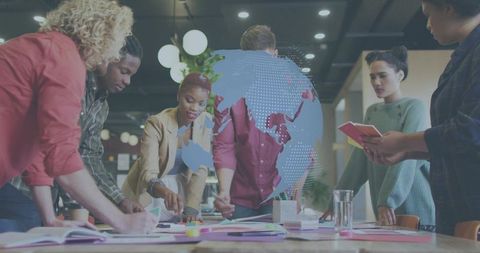 Creative team brainstorming around large table with digital globe overlay, coworking collaboration