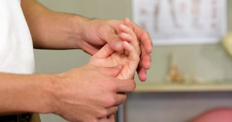Hand therapy clinician assessing finger joints and palpating palm for rehab