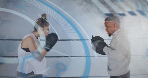 Female boxer training with coach holding mitts in boxing ring for technique and endurance