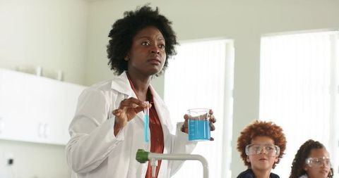 African woman teaching chemistry experiment in classroom lab with youth students observing