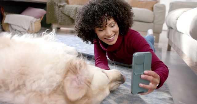 Woman lying on floor taking selfie with golden retriever, showcasing bond with pet. Indoor casual setting conveys warmth and joy. Ideal for social media, pet ownership blogs, lifestyle articles, dog-related content, promoting technology in everyday life.