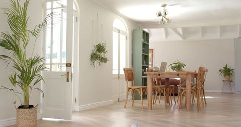 Sunlit minimalist dining and workspace with wooden table, rattan chairs, arched windows