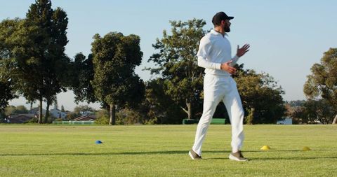 Cricket player walking between training cones on sunny suburban park field, copy space