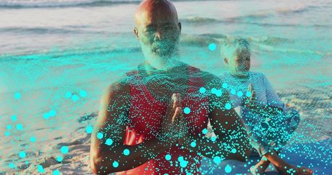 Meditating mature man at beach with turquoise particle overlay and partner behind