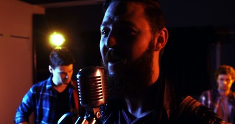 Male vocalist singing in studio with bandmates performing