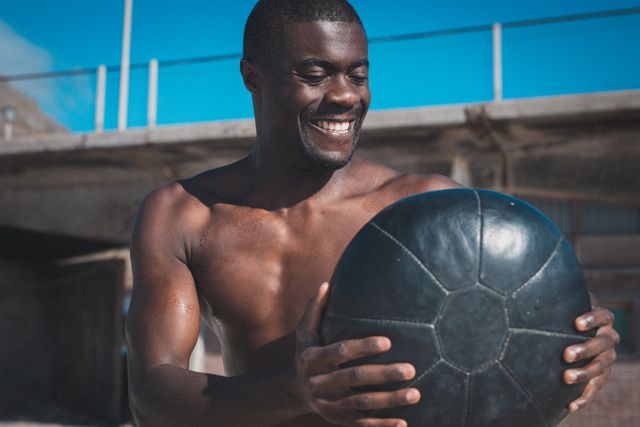 Portrait of smiling african american man exercising with weights on sunny day. healthy outdoor lifestyle fitness training.