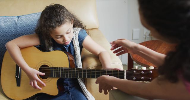 Happy biracial mother and daughter playing with guitar. domestic life and family leisure time concept.
