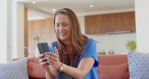 Mature Asian Woman Smiling While Using Smartphone in Cozy Living Room