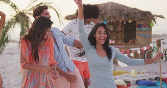 Happy group of diverse friends dancing on beach by beach bar at sundown. Summer, free time, friendship, party, celebration and vacations.