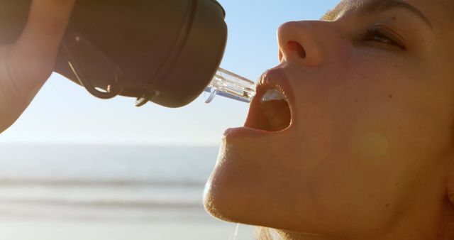 Caucasian woman drinking water from bottle on beach at sundown. Travel, tranquillity, nature, vacations and lifestyle, hydration, unaltered.