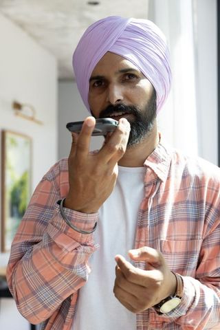 Indian Man Using Smartphone Speaker in Sunlit Interior