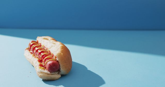 Hot dog bun with sausage, mustard, and ketchup, on light blue backdrop. Perfect for fast food advertisements, culinary blogs, or dining menus. Bright background emphasizes simple presentation, suitable for social media content and promotional materials.