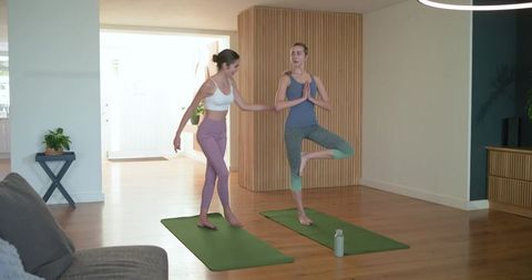 Instructor guiding student through tree pose home yoga session in bright living room