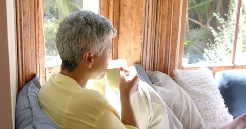 Senior Woman Relaxing with Tea by Sunlit Window in Cozy Home
