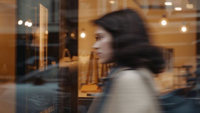 Woman walking past boutique window with handbags and warm reflections