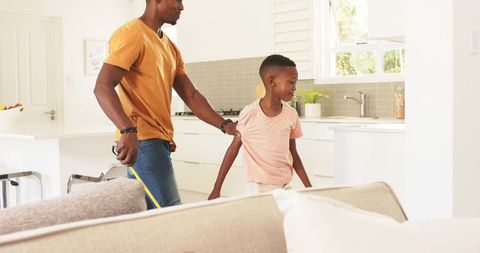 African american father measuring and guiding son in bright modern kitchen renovation
