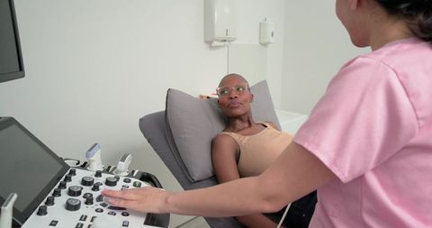 Diverse nurse performing ultrasound on older woman reclining in clinic